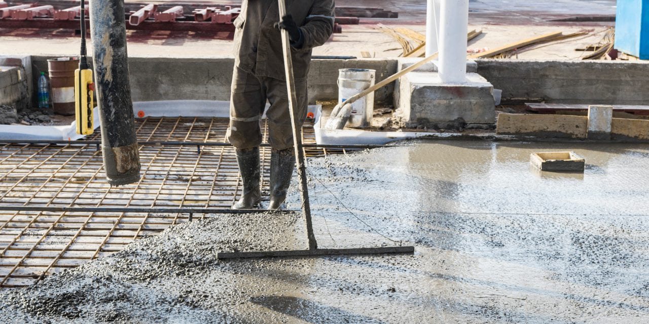 Construction worker leveling a poured concrete floor in an industrial workshop. Legs in boots in concrete. Surface concreting. Monolithic reinforced concrete works
